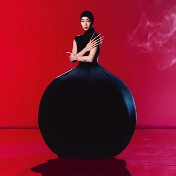 Cover of Hold the Girl by Rina Sawayama, featuring Rina with extremely long fake nails, posed with arms folded across her chest, one arm hold the elbow of the other one, which lays diagonally across her torso. She is in an all black suit that covers her head except her face and goes down into an orb shape that covers her legs completely. The background is vibrant red with a wisp of smoke to the upper right corner of the frame.